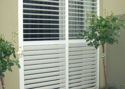 White plantation shutters opened behind plants